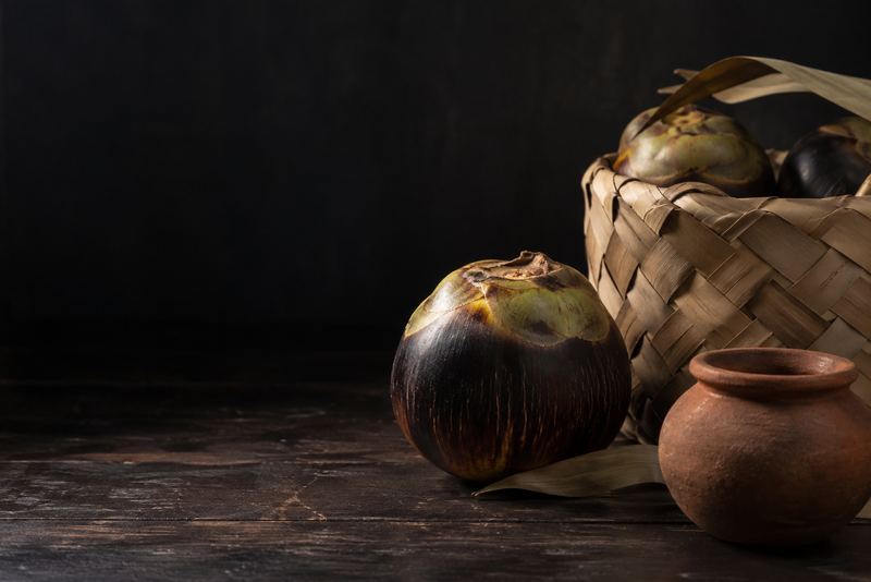 A palmyra fruit, a woven palmyra-leaf basket and a small clay pot on dark wood, warm light