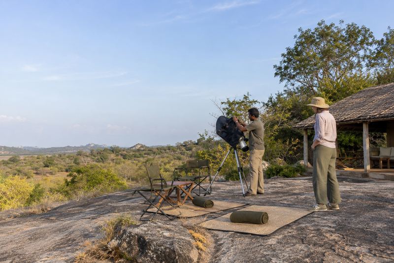 A guide setting up a telescope on a sunlit dry-zone rock