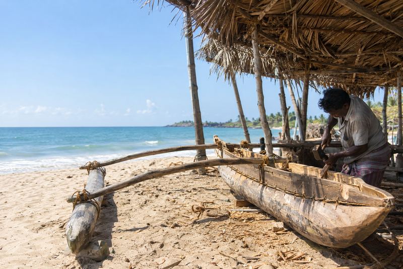 An oruwa outrigger canoe being built on a sunny beach