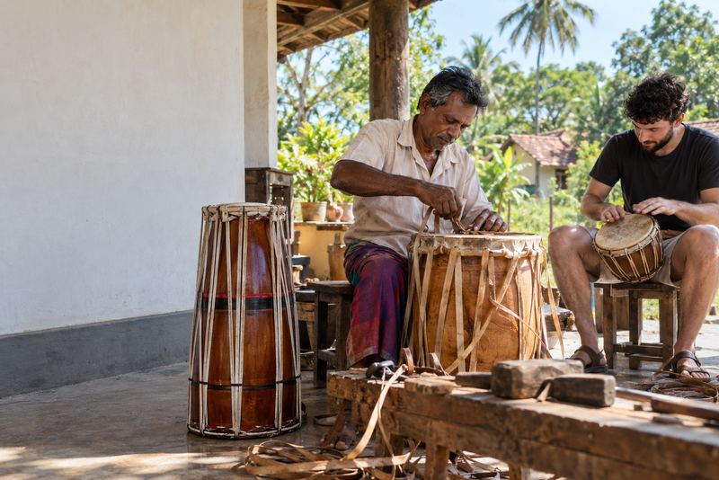 A drum-maker lacing a drum while a visitor tries another