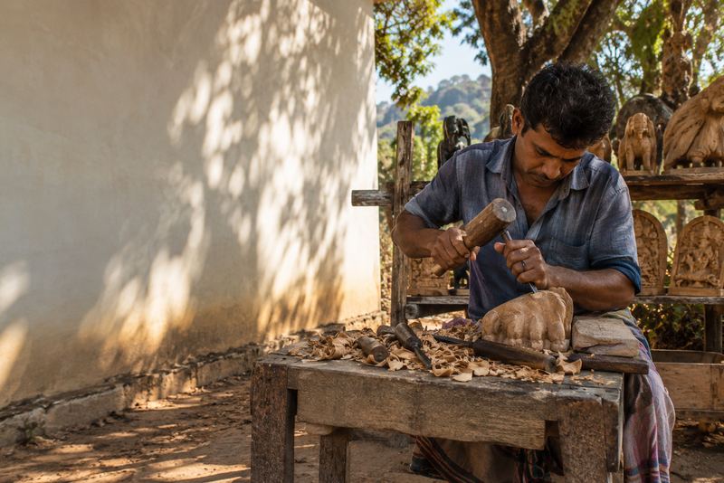 A carver finishing a wooden Lion's Paw carving outdoors