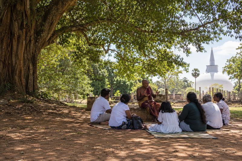 A storyteller with listeners under a tree near a dagoba