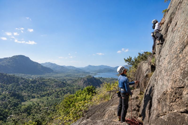 A climbing instructor belaying a learner on sunny granite