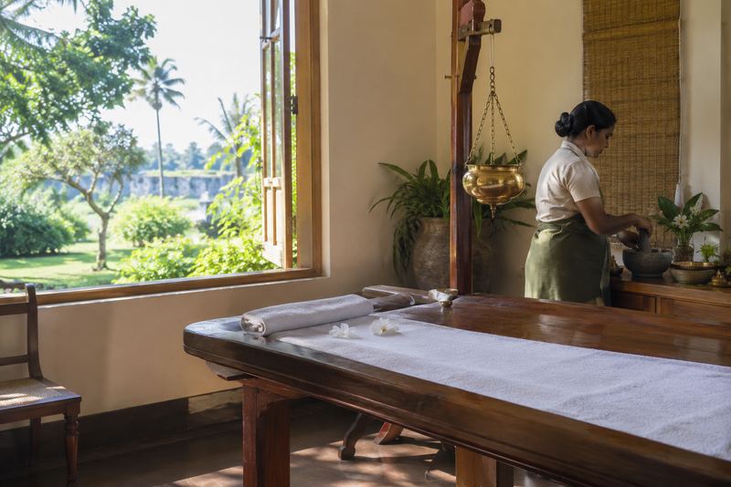A sunlit Ayurvedic treatment room with a practitioner preparing herbs