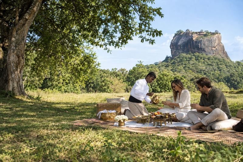 A picnic on a woven mat with Sigiriya rock beyond in sunshine