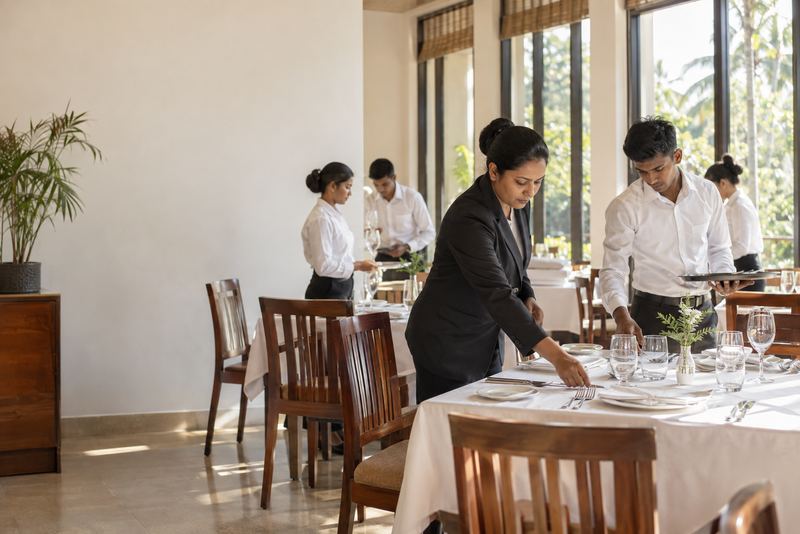 Hospitality trainees laying a table in a sunlit training restaurant