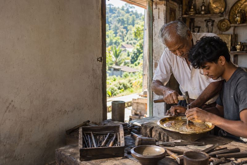 A master guiding an apprentice chasing a brass tray