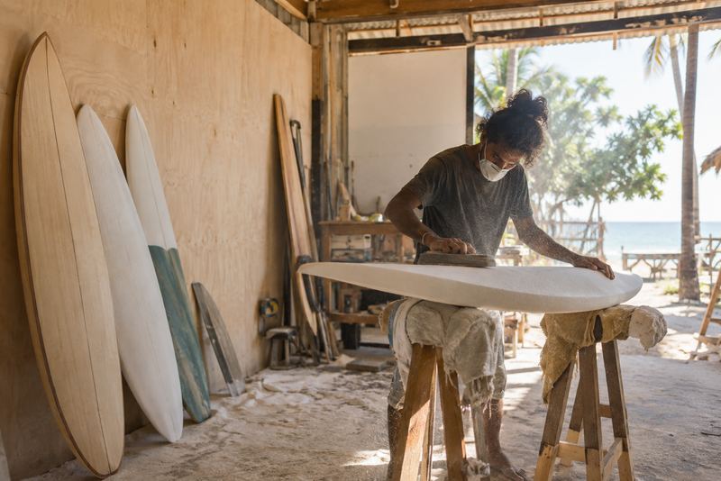 A shaper sanding a surfboard in a sunny workshop