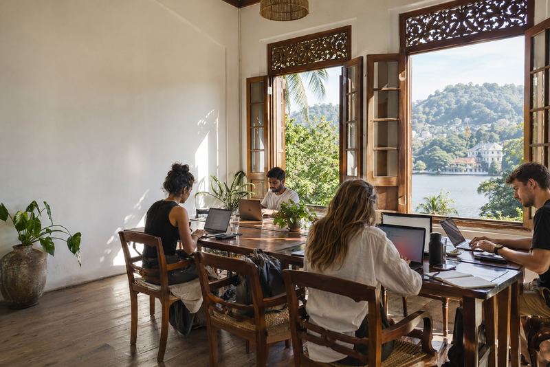 People working at long tables in a sunny Kandy house