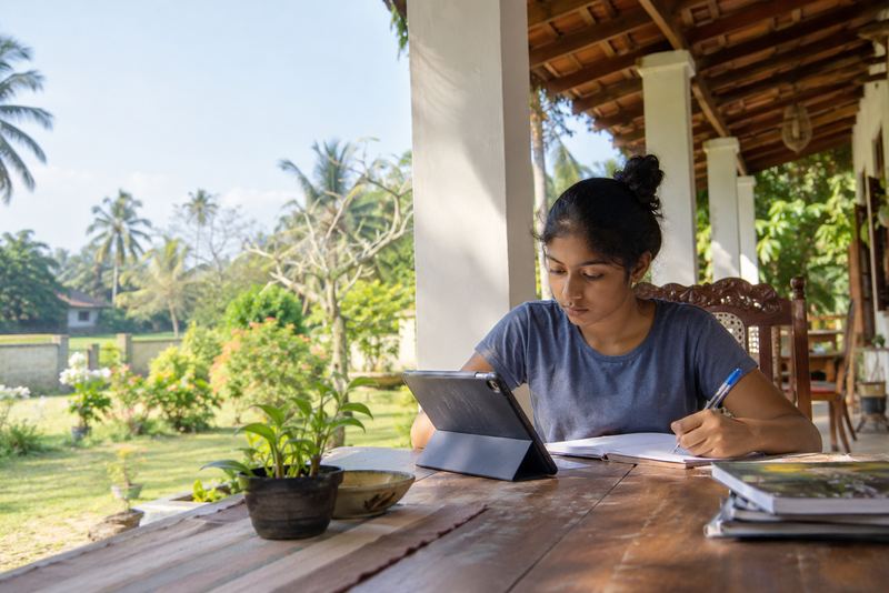 A teenager studying from a tablet on a sunny veranda