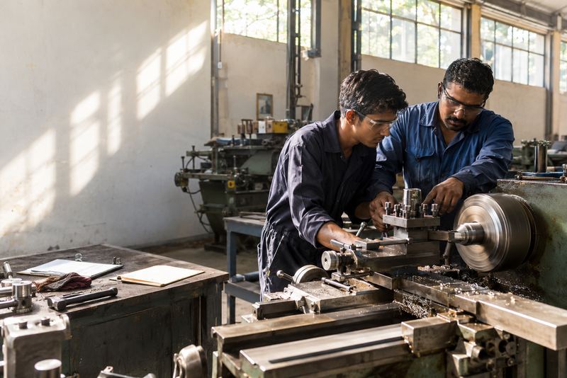 An apprentice at a lathe with a machinist guiding him
