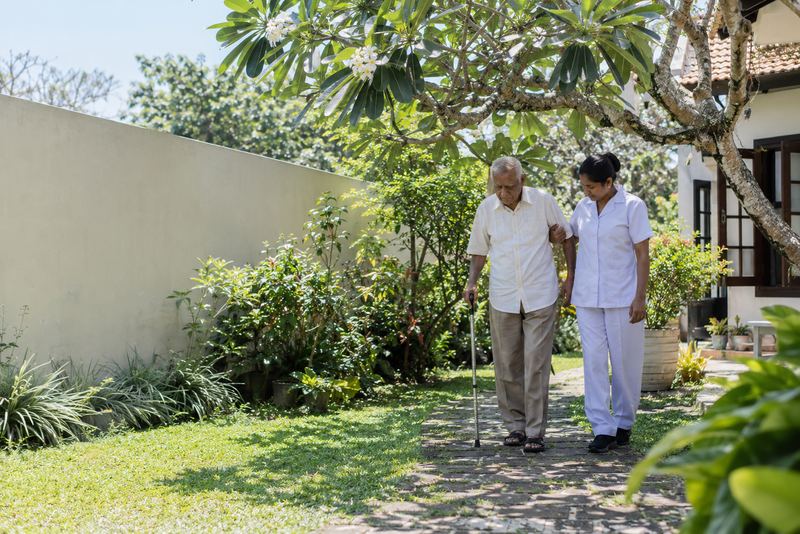 A carer helping an elderly man walk in a garden