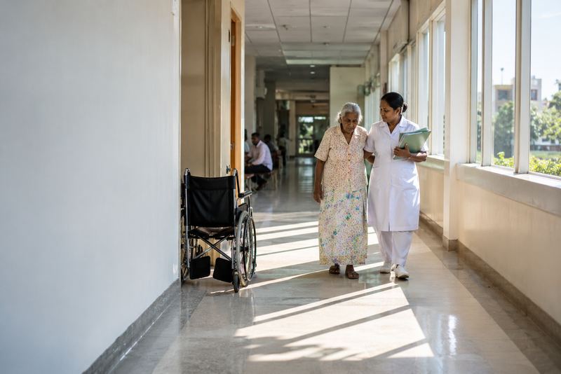 A nurse escorting an elderly parent along a hospital corridor
