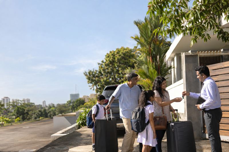 A returning family with suitcases at the gate of a house