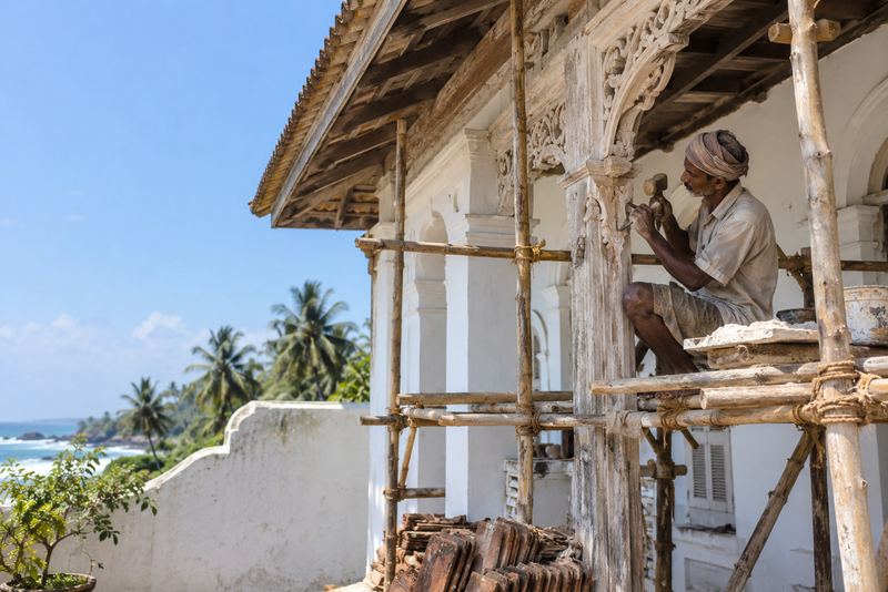 A restorer repairing a carved villa veranda in bright sun