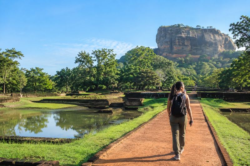 A visitor with earphones walking towards Sigiriya rock in sunshine