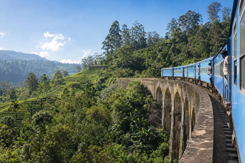 A restored blue train crossing a stone bridge in tea country
