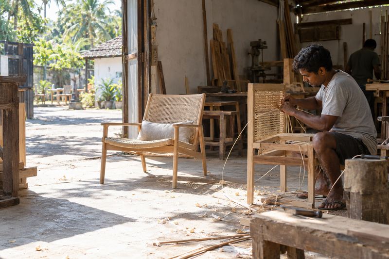 A craftsman weaving rattan chairs in a sunny workshop