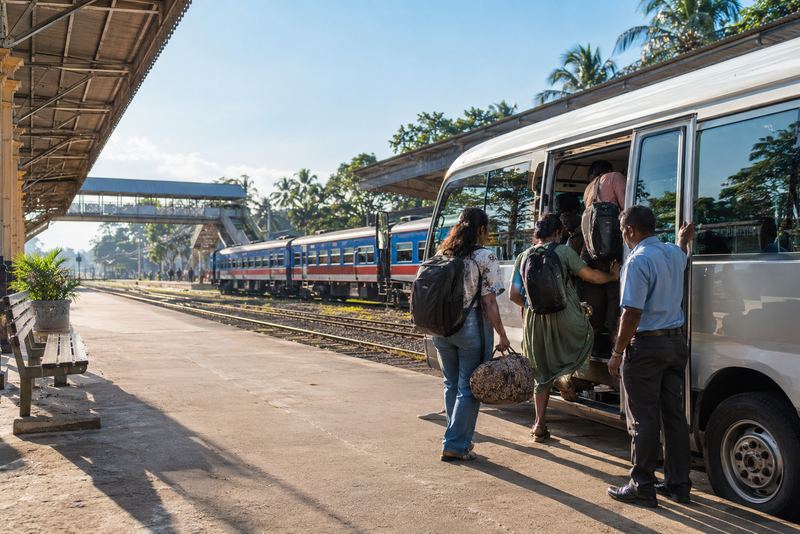 Passengers boarding a minibus at a sunny railway station