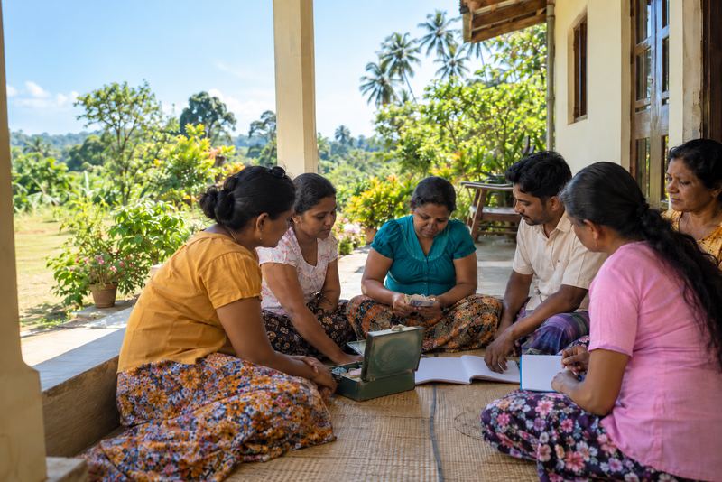 A village business group counting loan money on a sunny veranda
