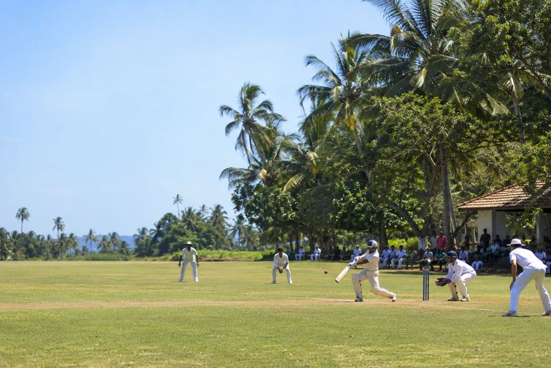 A visiting club team fielding on a sunny palm-ringed ground