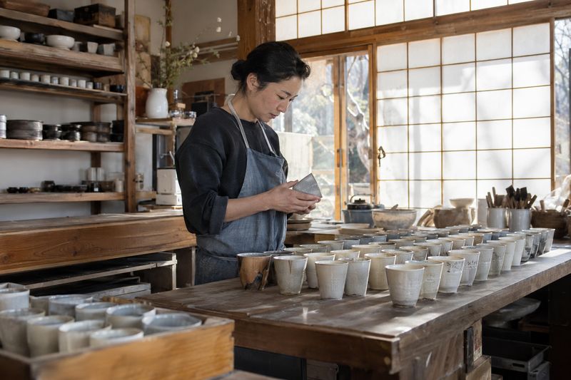 An inspector checking finished cups one by one in a small Japanese pottery workshop