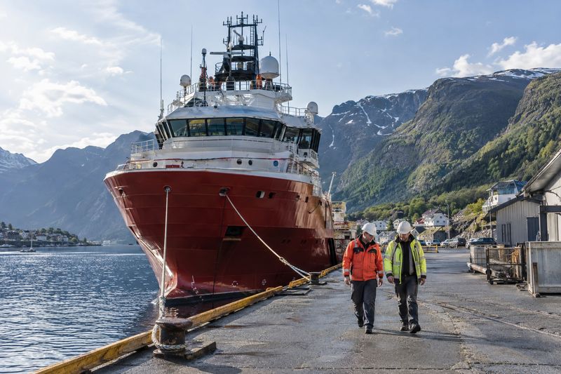 A fjord harbour in Norway with a supply ship at the quay and engineers walking past