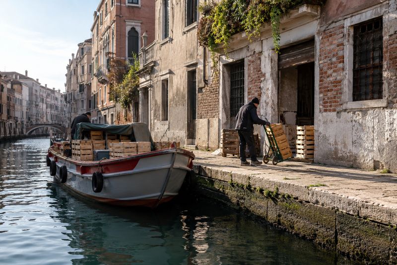A cargo boat unloading crates on a quiet working canal in Venice